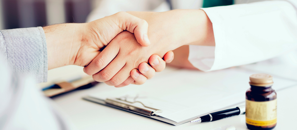 patient shaking hands with health care provider over desk